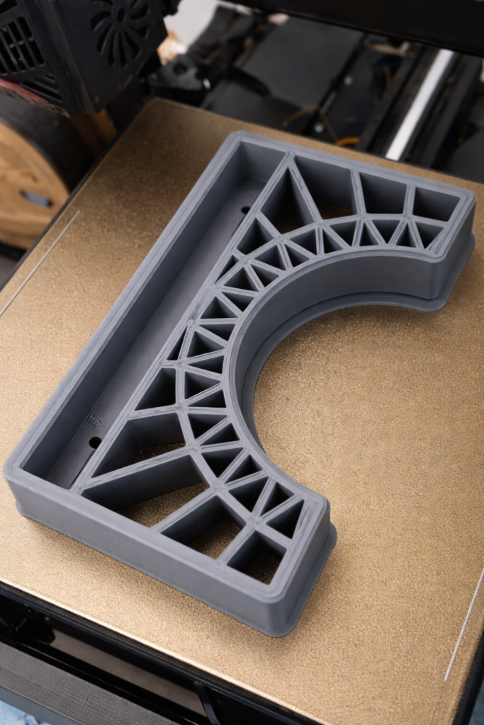 Grande pièce technique grise imprimée en 3D en cours de fabrication sur imprimante 3D.